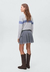 Siv pulover z modrimi črtami, krilo s pikami in rjave antilop čevlje do kolen, prikazano s hrbtne strani v svetlo sivi okolici.