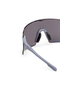 Okulary przeciwsłoneczne z dużą, zakrzywioną ciemną soczewką, szarymi plastikowymi oprawkami i gumowymi czarnymi noskami. Posiadają teksturowany szary boczny zausznik.