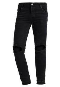 Jean skinny noir en denim, avec des découpes déchirées aux genoux, un design classique à cinq poches et un ourlet légèrement effiloché.