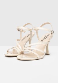 Witte lakleren hoge sandalen met meerdere kruislings bevestigde banden, een slanke enkelband en een 3-inch stiletto hak. Gladde en glanzende afwerking.