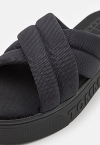 Sandale noire à glissière avec des brides en tissu croisées épaisses et rembourrées et une semelle épaisse avec un logo en relief sur le côté.