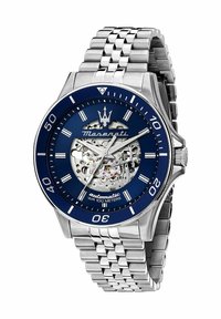 Silver stainless steel automatic watch with a blue dial, skeleton display, and textured bracelet. Water-resistant to 100 meters.