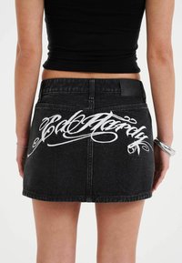 Black denim mini skirt featuring white embroidered lettering on the back, with a classic cut and a textured fabric finish.