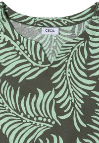 Haut vert avec motif de feuilles tropicales vert clair et une encolure en V, avec une étiquette blanche portant le nom de la marque "CECIL".