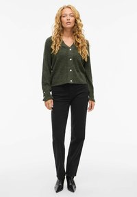 Groene gebreide cardigan met een V-hals, ronde knopen en lange mouwen, gecombineerd met zwarte rechte jeans en puntige zwarte enkellaarzen.