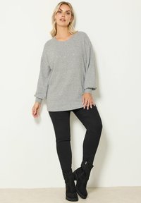 Sweatshirt gris avec un col rond et des détails embellis sur le devant, associé à un pantalon noir ajusté et des bottes noires jusqu'aux genoux.