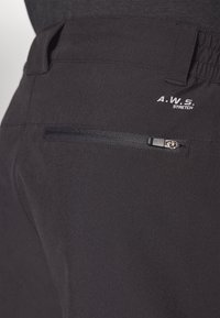 Svart stretchbyxor med en dragkedjeförsedd bakficka och broderad text "A.W.S. STRETCH". Slät textur, designad för flexibilitet och komfort.