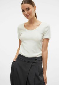 Witte geribde t-shirt met een ronde hals gematcht met donkergrijze hoge taillebroek met plooien en knoopsluiting.