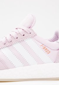 Rosa sneaker med vita zickzackmönster, mjukt texturerat tyg och vit gummisula. Har snören och en liten orange etikett (T-5923).