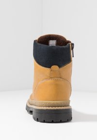 Stivaletto alla caviglia in pelle marrone con colletto in camoscio nero, suola in gomma e zip laterale. Presenta una fodera interna morbida.