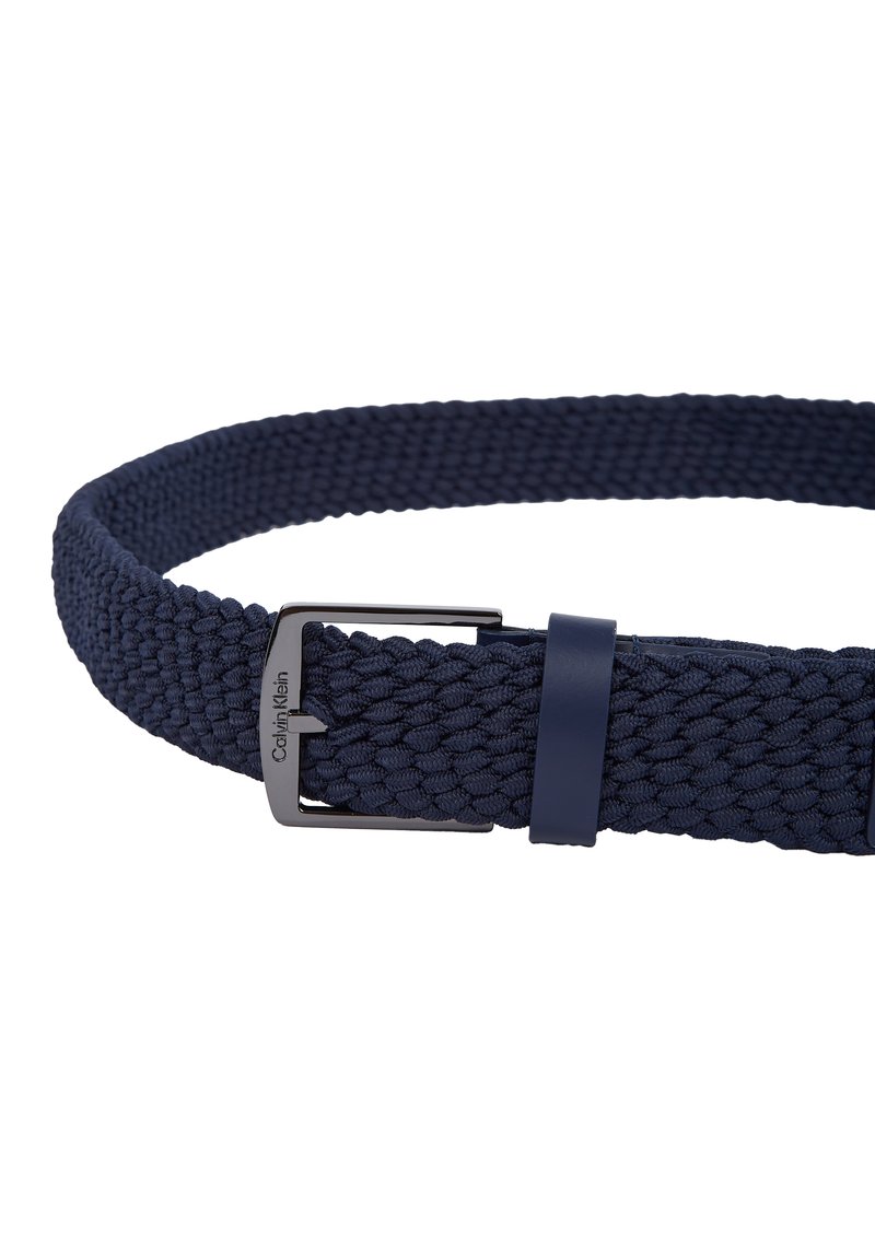 Cintura intrecciata blu navy realizzata in materiale elastico con una fibbia in metallo nera e un accento in pelle abbinato. Presenta una texture intrecciata in tutta la sua lunghezza.
