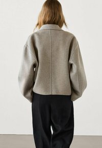 Szara, przerośnięta, wełniana kurtka z kołnierzem i opadającymi ramionami, z wyraźnym szwem z tyłu. Połączona z luźnymi czarnymi spodniami.