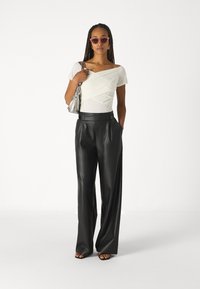 White off-shoulder top with textured wrap design, paired with high-waisted black faux leather wide-leg trousers and strappy black sandals.