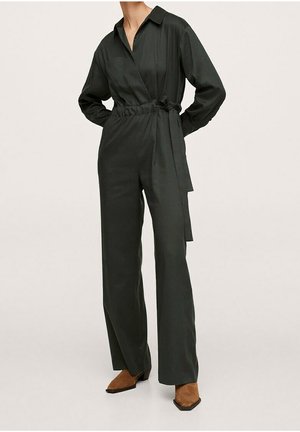 Black long-sleeve wrap jumpsuit with a waist tie, paired with brown pointed-toe boots, worn by a standing person against a plain background.