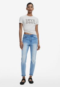 T-shirt grigio chiaro con la scritta "LOVE DSGL" in lettere scure, abbinata a jeans in denim blu leggermente usurati e scarpe nere slip-on.