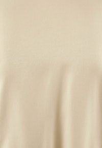 Ljus beige, slät tyg med en mjuk textur; inga tydliga mönster eller hårdvara synliga. Ytan verkar något reflekterande.