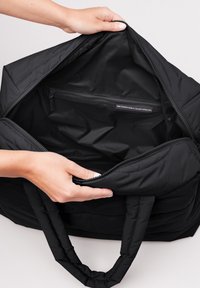 Svart tote bag med kviltad textur, dragkedjestängning och inre dragkedjefack. Tillverkad av återvunna fiskenät.