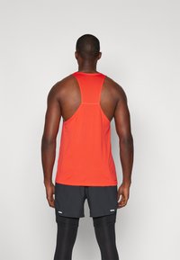 Camiseta deportiva roja sin mangas con diseño de espalda nadadora, fabricada en tejido ligero y texturizado, combinada con pantalones cortos y mallas negras.