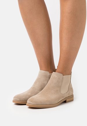 Botas de tobillo de ante beige con paneles laterales elásticos y puntera redonda. Tacón bajo apilado y suela lisa para un uso cómodo.