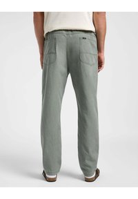 Vihreät puuvillahousut rentoa mallia, joissa on kaksi takataskua, näkyviä ompelulankoja ja kevyesti kapenevat lahkeet.