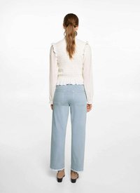 Biely smockovaný top s volánmi, skombinovaný so svetlomodrými vysokými nohavicami s širokými nohavicami. Model má na sebe hnedé sandále na podpätku.