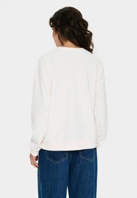 Sweatshirt rose clair avec un col rond, des manches longues et des poignets côtelés. Porté avec un jean bleu ample, montrant une vue arrière simple.