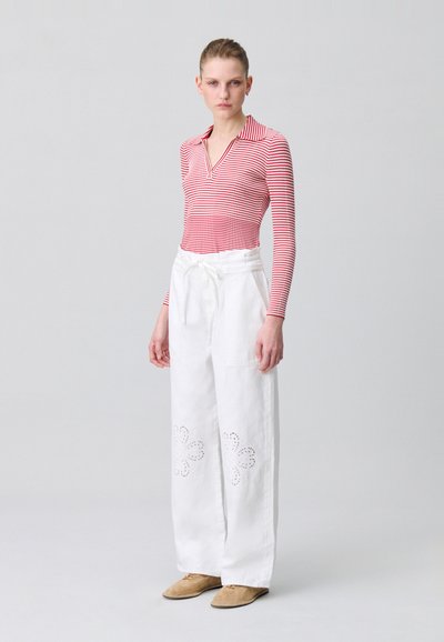 Top de rayas rojas y blancas de manga larga con escote en V; pantalones anchos blancos con detalles de ojete floral; calzado marrón claro.