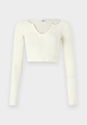 Crop top in off-white knit material. Long sleeves with ribbed texture and small cut-out details around the neckline.