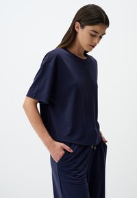 T-shirt blu navy a maniche corte con vestibilità ampia, scollo rotondo e texture liscia. Indossato con pantaloni coordinati dotati di tasche laterali.