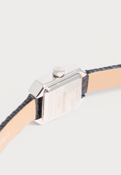Vue arrière d'une montre-bracelet rectangulaire argentée avec un bracelet en cuir noir et une doublure intérieure beige sur fond blanc.