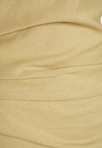 Stretchigt beigefärgat tyg med en ribbad textur, med en samlad design som skapar mjuka veck och konturer över ytan.