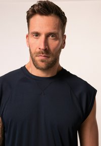 Ärmlös idrottströja i marinblått tillverkad av slät tyg med rund hals och raglan-sömmar, med en avslappnad passform och minimalt sömnadsdetaljer.