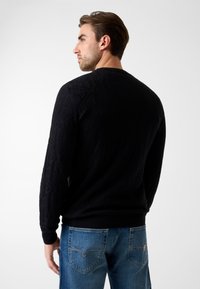 Zwarte gebreide trui met een gestructureerd geometrisch patroon, ronde halslijn en geribbelde boorden, gecombineerd met lichtblauwe denim jeans.