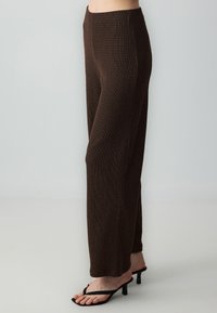Pantalons marron texturé, ample, avec une taille haute, de subtils lignes verticales et une conception à jambe droite. Associés à des sandales à talons noires.