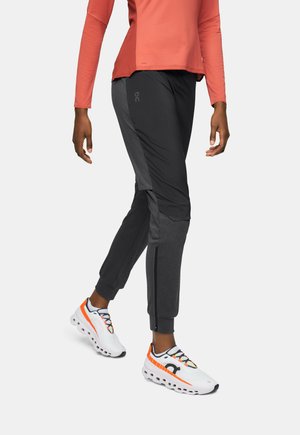 Svarta och grå sportbyxor med smal passform, med sidofickor med dragkedja och logodetalj. Matchas med vita sneakers med orange detaljer.