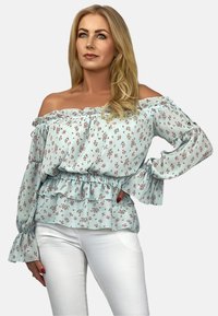 Bluzka na ramiączkach w jasnoniebieskim kolorze z kwiatowym wzorem, z falbankami u rękawów oraz przewężoną talią. W zestawieniu z białymi spodniami.