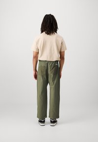 Beige bomulls t-shirt med korta ärmar, tillsammans med löst sittande, olivgröna byxor med två bakfickor, bärs med svarta sneakers.