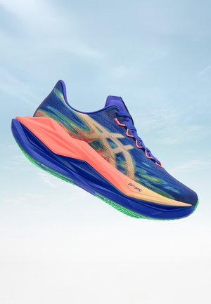 Blauer Laufschuh mit grünen und korallenfarbenen Akzenten, einer dicken korallenfarbenen Sohle und einem beigen Logo an der Seite, schwebt vor einem hellen Himmelshintergrund.