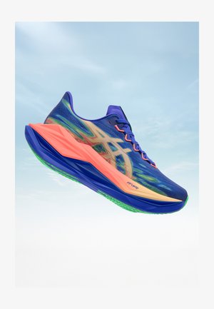 Blauer Laufschuh mit grünen und korallenfarbenen Akzenten, einer dicken korallenfarbenen Sohle und einem beigen Logo an der Seite, schwebt vor einem hellen Himmelshintergrund.