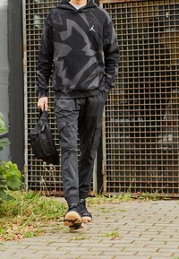 Haut à capuche noir avec des motifs géométriques, poche avant, associé à un pantalon fuselé assorti avec des poches cargo. Portant un sac noir.