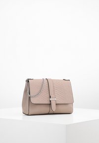 Borsa beige con patta testurizzata, chiusura in argento e tracolla a catena esposta su un piedistallo bianco contro uno sfondo semplice.