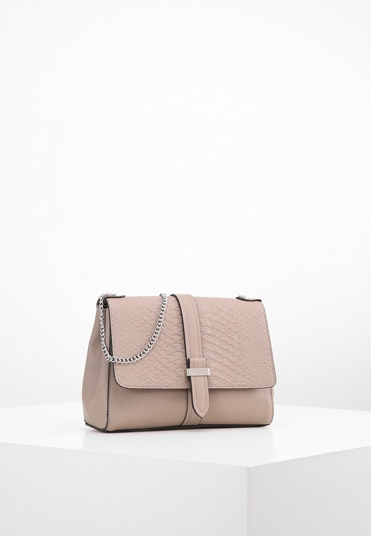 Borsa beige con patta testurizzata, chiusura in argento e tracolla a catena esposta su un piedistallo bianco contro uno sfondo semplice.