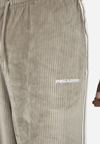 Beige Cordhosen mit vertikaler Rippstruktur, Kordelzugbund, seitlichen Streifen und gesticktem "PEGADOR"-Logo in Weiß.