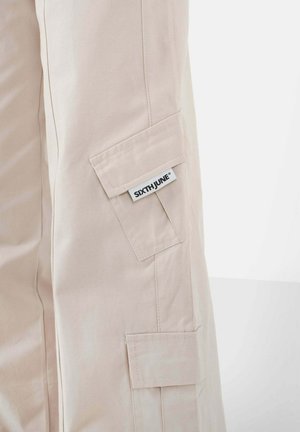 Beige Cargo-Hosen mit zwei Seitentaschen, aus Baumwollmaterial gefertigt. Mit einem Etikett mit dem Markennamen "SIXTHJUNE" an der Seite.