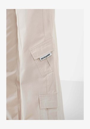 Beige cargo pants with two side pockets, made of cotton material. Features a label with the brand name "SIXTHJUNE" on the side.