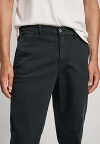 Tumedad hallid, puuvillast valmistatud chinosid, millel on sile tekstuur, sirge jalgade disain, küljetaskud ja nööbiga kinnitamine vöökoht.