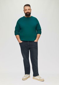 Jeans bleu foncé, pull sarcelle, baskets claires. Coupe décontractée, col rond, poignets côtelés et tissu texturé. Design simple, sans motifs.