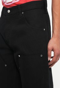 Melni denim bikses ar pieguļošu siluetu, kas aprīkotas ar sānu kabatām un sudraba furnitūru. Strukturēts audums ar vienkrāsainu dizainu.