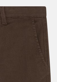 Pantalons en tissu marron avec une texture lisse, une taille standard et des poches avant avec des détails de couture subtils.