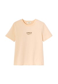T-shirt à manches courtes de couleur pêche en coton doux. Il possède un col rond et un texte marron centré "AMOUR toujours" sur le devant.